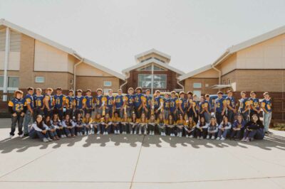 2023 football and volleyball team members in front of main entrance of school