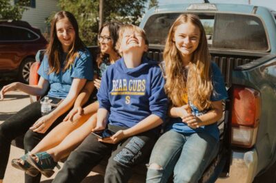 girls sitting on tailgate of truck to watch the homecoming parade