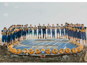 2023 high school boys football team pose for team pictures around the rock art S located on hillside near school